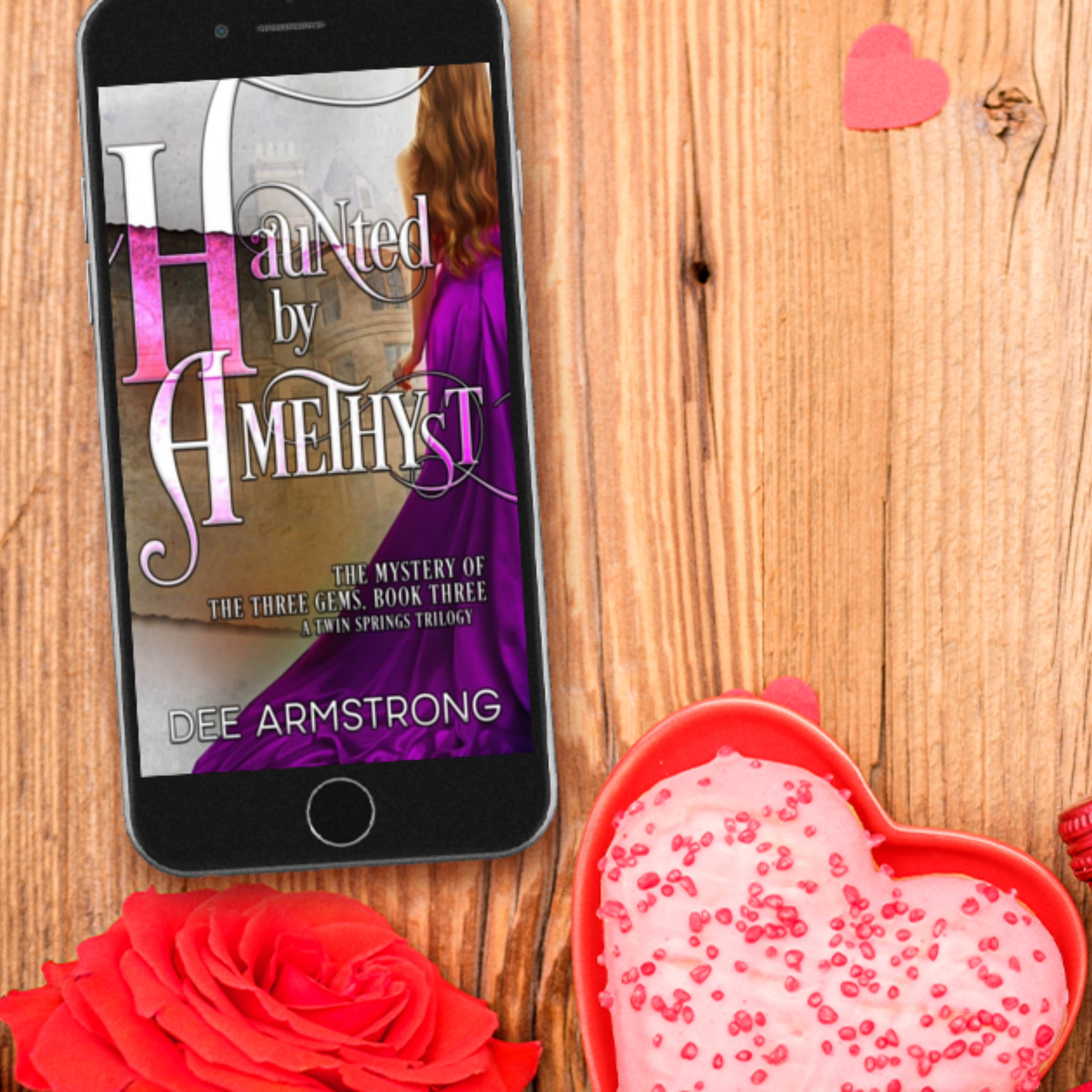 Phone displaying 'Haunted by Amethyst' book cover on a wooden surface with decorative items.