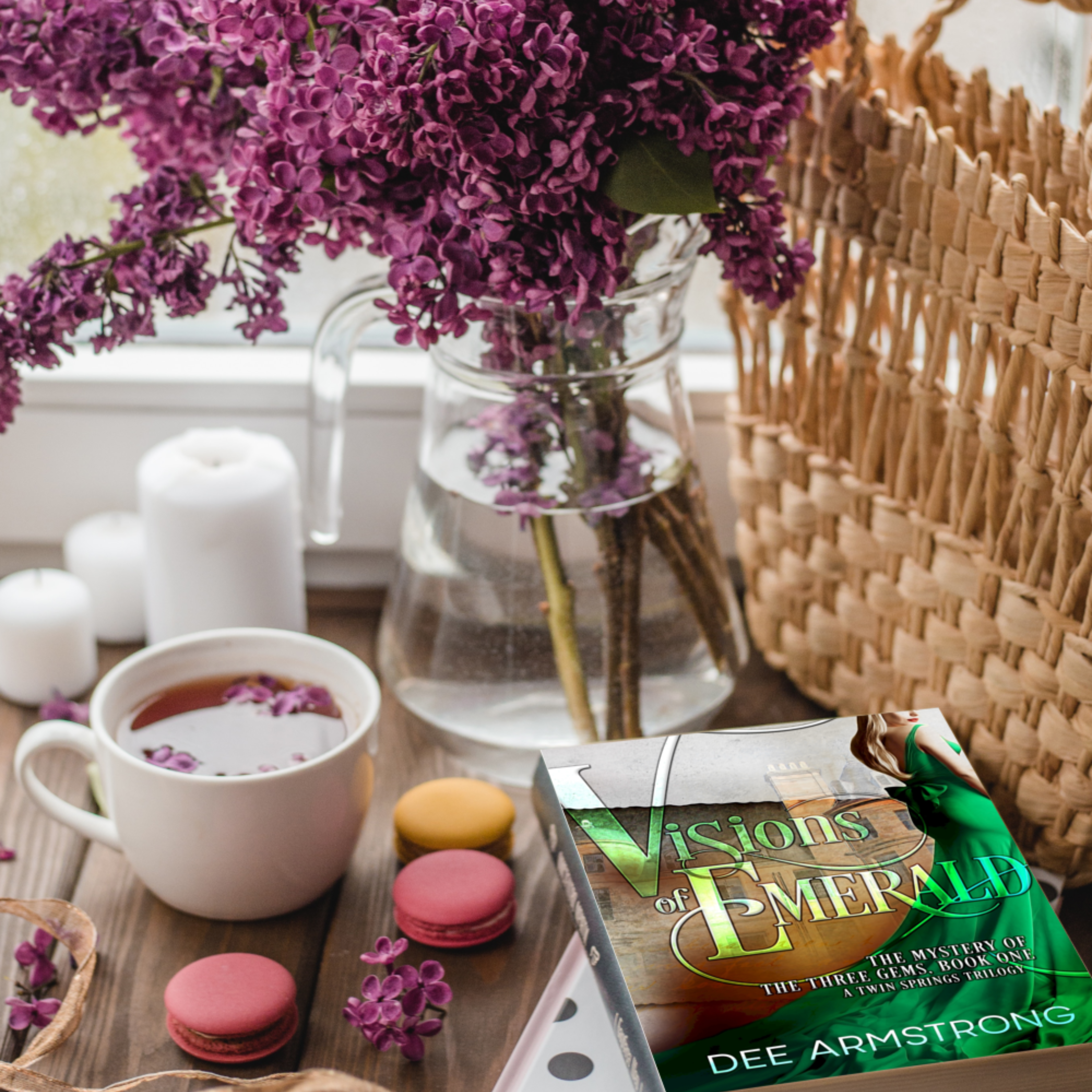 Book titled 'Visions of Emerald' by Dee Armstrong on a table with a cup, cookies, and flowers.