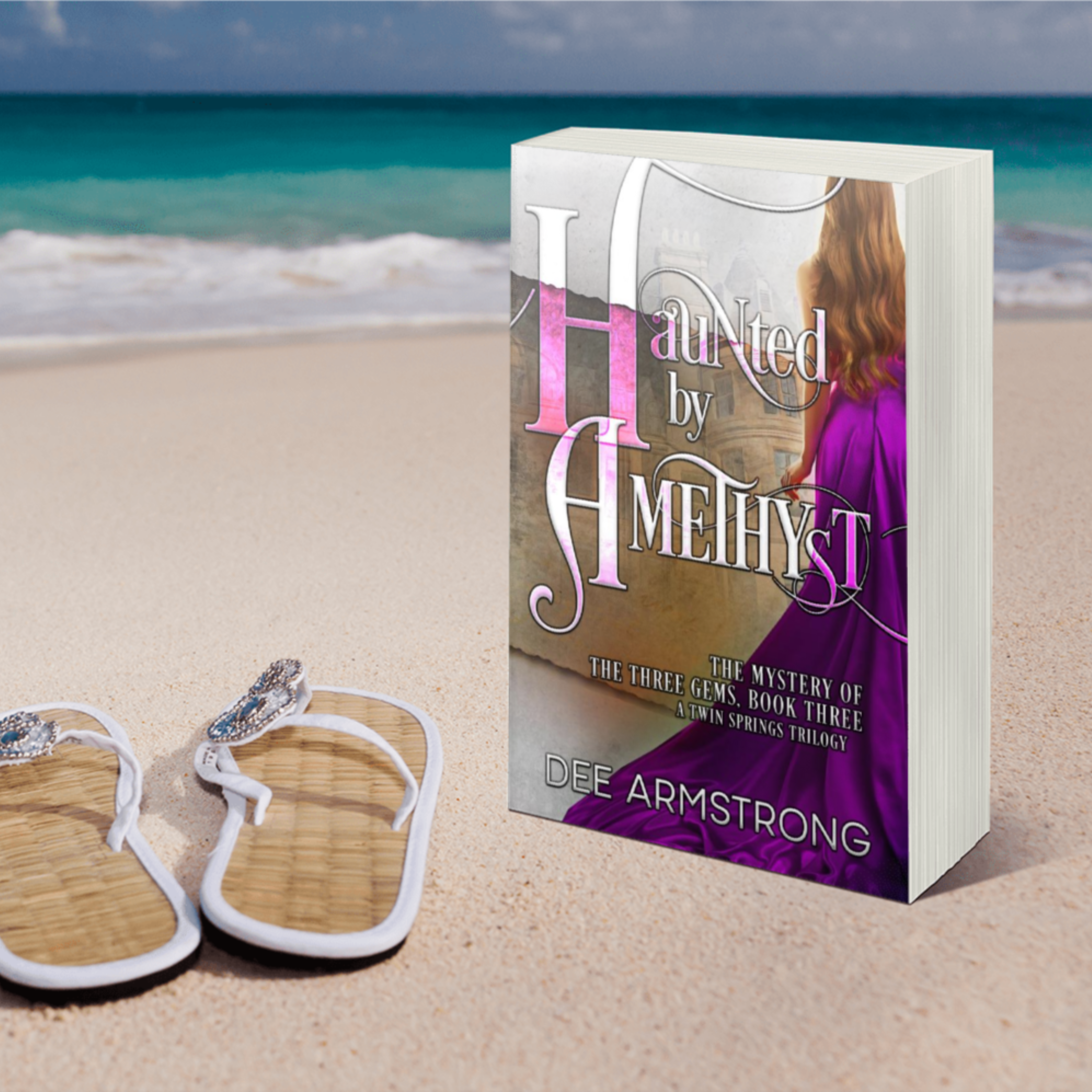 Book titled 'Haunted by Amethyst' by Dee Armstrong on a beach with sandals and ocean view