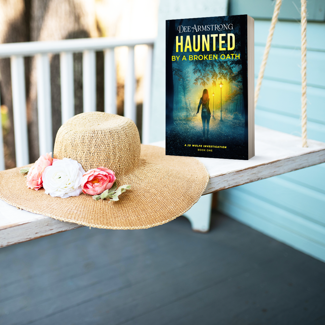 Book titled 'Haunted by a Broken Oath' by Dee Armstrong on a swing with a sun hat and flowers.