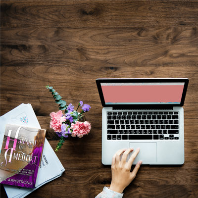Laptop on a wooden desk with the book Haunted by Amethyst and flowers