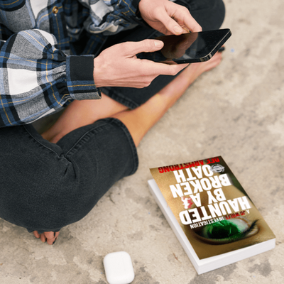 Person using a smartphone with a book titled 'Broken Oath' on the ground.