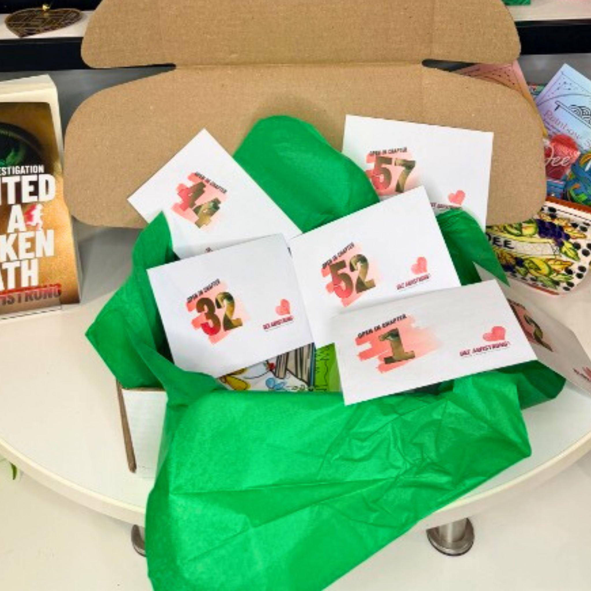 Cardboard box with green tissue paper and Open on Chapter envelopes on a table.