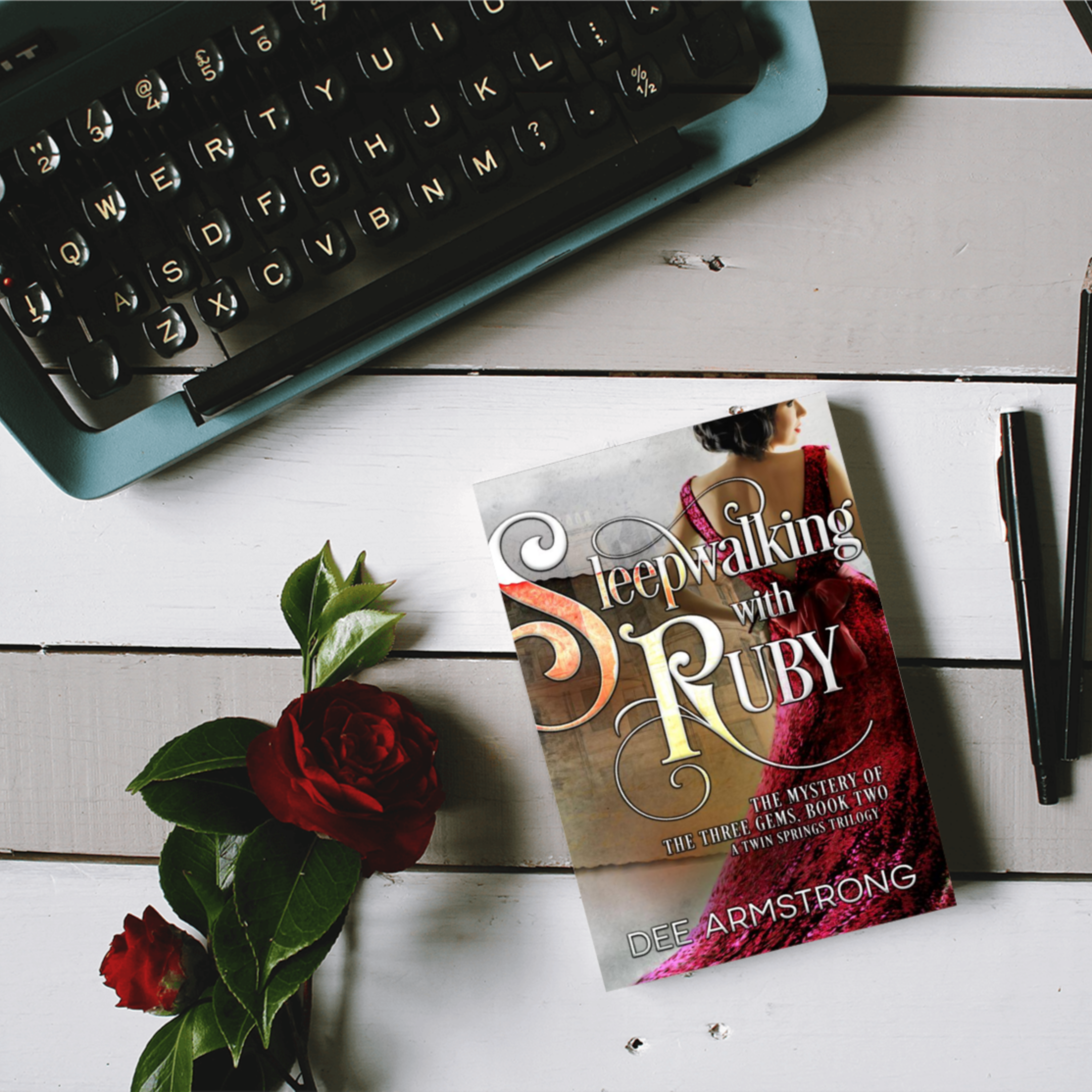 Book titled 'Sleepwalking with Ruby' by Dee Armstrong on a wooden surface with a typewriter and rose.